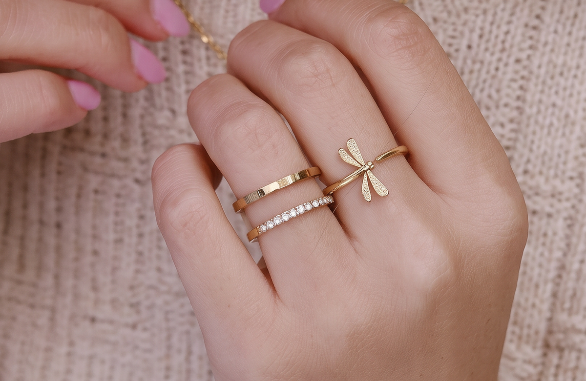 Libellula-Ring und goldene Ringe vor cremefarbenem Strick
